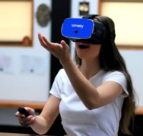 A student wearing the umety-branded VR headset, speaking and gesturing confidently while practicing a conversation